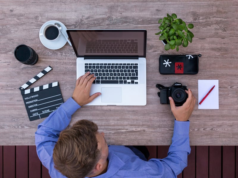 Video producer working at a laptop with a clapboard and DSLR camera nearby