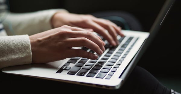 Person writing a blog on a laptop while paying attention to long-tail keywords and buyer personas to increase audience engagement.