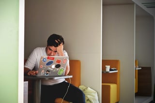 Man sitting at a table in front of a laptop computer with hands in hair to depict the frustration when you buy an article that's poorly written