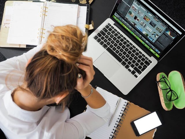 A woman looks at notes and a computer in frustration